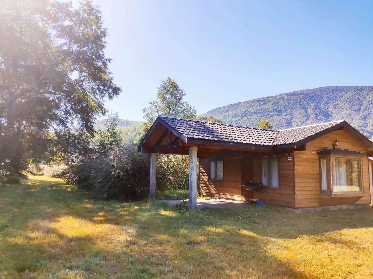 Cabaña de madera con terraza techada y cerros de fondo